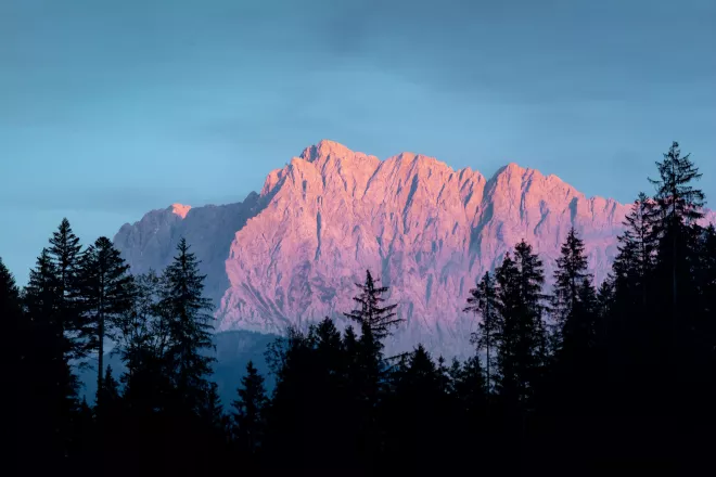 Mountain bathed in alpenglow, with the pinkish glow of the setting or rising sun reflecting off the mountain's surface.