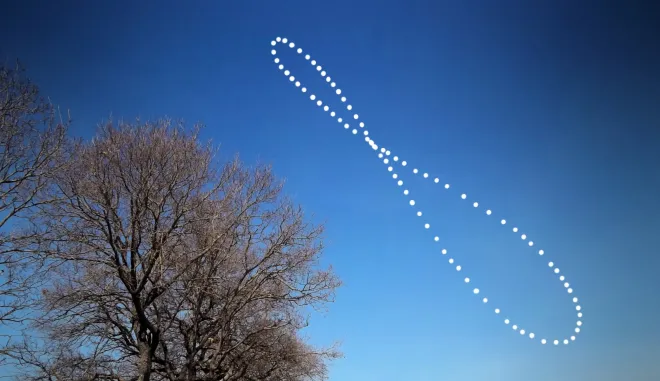 The Sun photographed at the same clock time through a year, tracing a figure-eight analemma over bare trees and a blue sky.