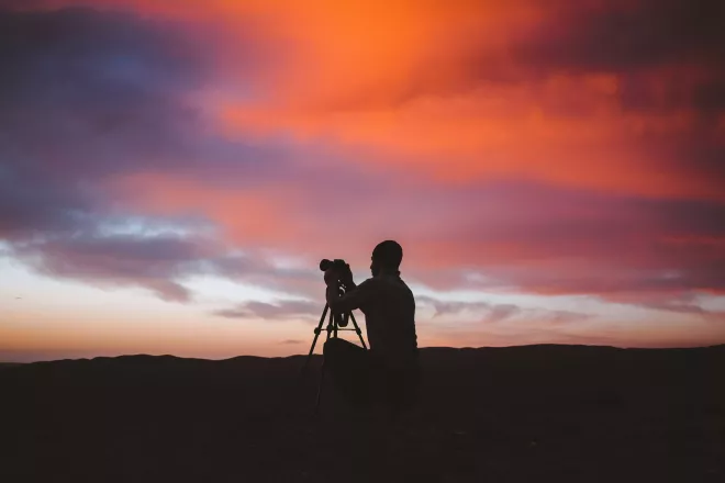 Photographer setting up his camera, silhouetted against a vibrant sunset sky