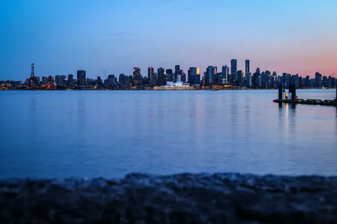 A city skyline across the water under a deep blue sky with a last pink glow.